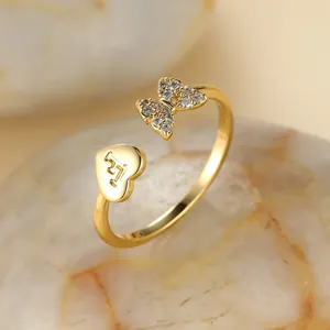 Détail macro de bague papillon dorée avec ailes en zircon et cœur gravé de la lettre F