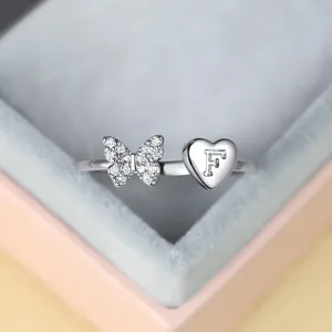 Détail macro d'une bague argentée avec papillon en cristal et cœur gravé lettre F