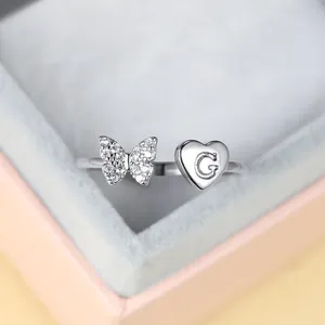 Vue détaillée d'une bague argentée ajustable avec papillon serti et médaille cœur lettre G