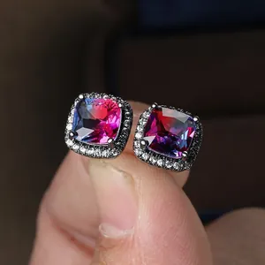 Macro detail of square halo earrings with multi-color gradient stones held by fingers