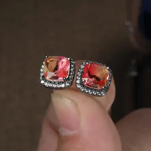 Macro view of halo square stud earrings with orange gemstone and black gold plating