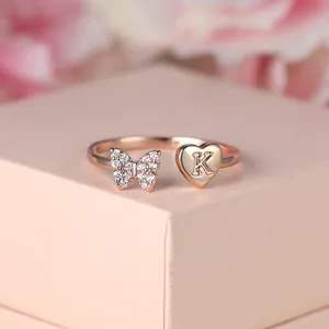 Gros plan d'une bague or rose avec papillon pavé et détail de cœur avec la lettre K