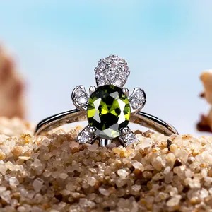 Macro shot of silver turtle ring with olive green gemstone on a beach sand background
