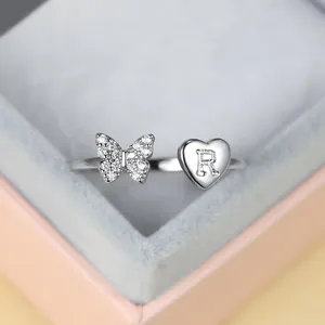 Détail d'une bague argentée papillon en zircon et cœur gravé avec la lettre R personnalisée