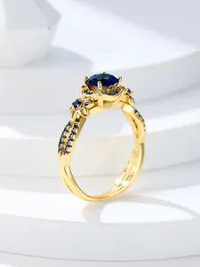 Detalle de anillo de oro rosa con piedra azul zafiro y banda con diseño entrelazado