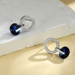 Gros plan de boucles d'oreilles géométriques avec zircon bleu sur pierre texturée