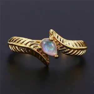 Macro shot of a golden feather ring featuring a pear-shaped opal stone against a black background