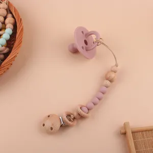 Attache-tétine en silicone rose avec perles en hêtre sur fond rose doux