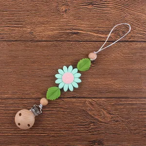 Détail de l'attache-tétine en bois avec fleur en silicone et perles sur fond en bois