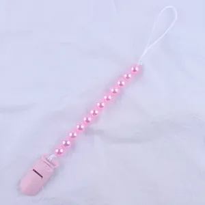 Detailed view of pink beaded pacifier clip with secure plastic clasp on white fabric