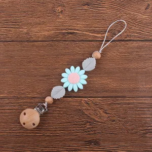 Détail de l'attache-tétine avec une marguerite en silicone bleu clair et des perles en bois de hêtre