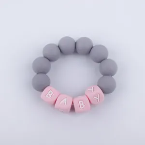 Macro detail of silicone baby teether bracelet with grey beads and pink letters spelling BABY