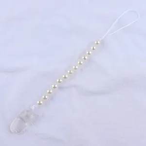 Detail of baby pacifier clip with white faux pearls and transparent plastic clamp