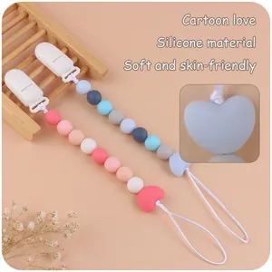Dettaglio delle catenelle per ciuccio in silicone con perle a cuore su sfondo caldo