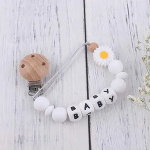 Detail view of baby pacifier clip with silicone daisy flower and wood beads on wood background