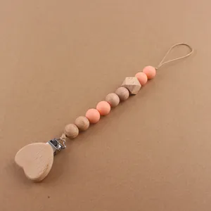 Detail of wooden heart pacifier clip with silicone beads on a brown background