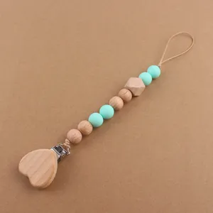 Close-up of wooden heart pacifier clip with mint green silicone beads on warm background