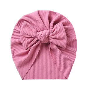 Detail of baby pink turban hat featuring ribbed fabric texture and a large soft bow