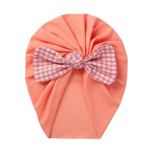 Detail of coral orange baby turban hat featuring a red and white checkered bow tie