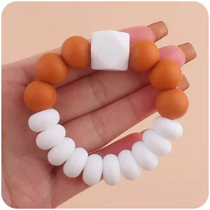 Nahaufnahme eines Beißrings aus Silikon mit orangefarbenen und weißen Perlen in der Hand