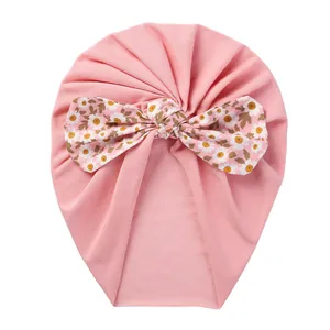 Detail of baby pink turban hat featuring a large floral daisy pattern bow for infants