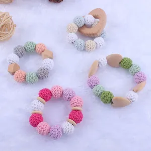 Infant beech wood heart teether with colorful macaron crochet beads on plush background