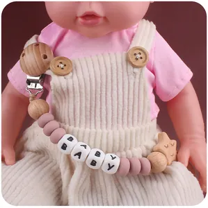 Detail von Schnullerkette aus Holz mit Stern und Silikonperlen an Babykleidung befestigt