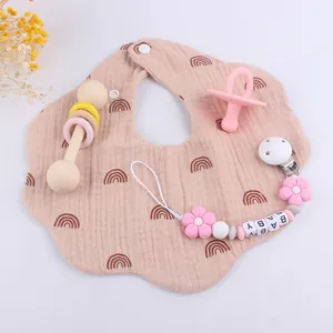 Flat lay of pink rainbow baby bib with silicone flower pacifier clip and wood rattle