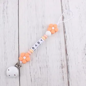 Detail of baby pacifier clip with silicone flowers, letter beads, and secure white clamp