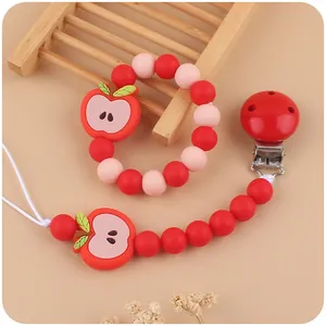 Detail of red apple silicone pacifier clip and teething bracelet on a wooden decor