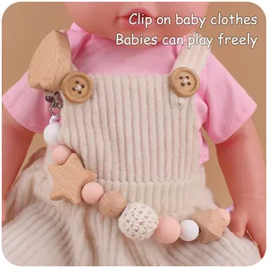 Detail of baby pacifier clip with beech wood stars and pink silicone beads on doll clothing