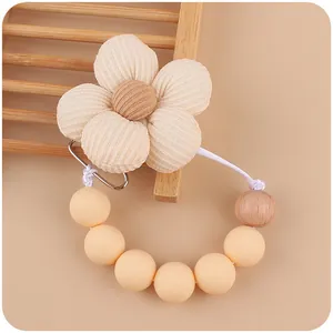 Detail of baby pacifier clip with beige fabric flower, wooden beads, and metal clasp