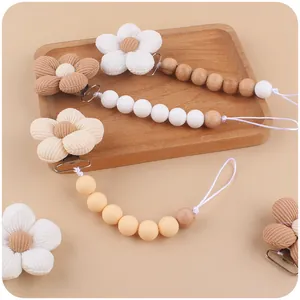 Baby pacifier clips with silicone beads and fabric flowers on a wooden tray