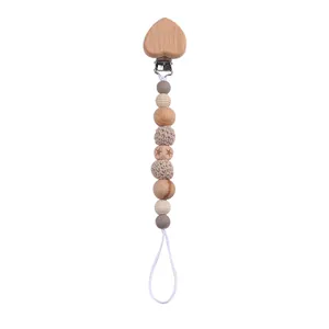 Detail of baby pacifier clip with heart wooden clip and natural beads on white backdrop