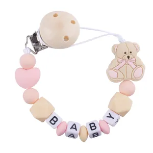 Macro view of pink silicone beads and wooden clip with a cute cartoon bear and baby letters