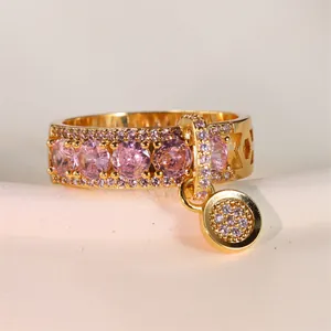 Détail d'une bague dorée avec zircons roses, motif nid d'abeille et pendentif rond