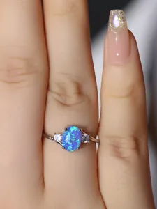 Primo piano di un anello in argento con opale blu ovale e zirconi sulla mano