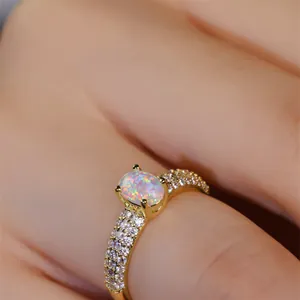 Close-up of a gold ring with an oval opal stone and pave-set cubic zirconia on hand