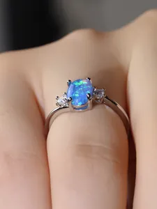 Primo piano di un anello in argento con opale blu ovale e zirconi indossato al dito