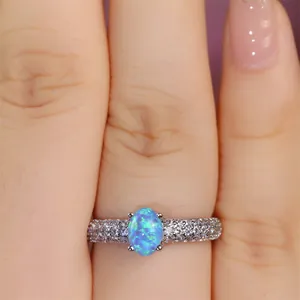 Detailed view of an oval blue opal ring with pave-set cubic zirconia on a woman's finger