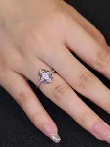 Detalle de un anillo de opalo ovalado plateado con halo de diamantes en un dedo