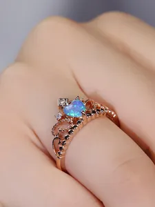 Macro detail of crown ring featuring heart-shaped opal and rose gold plating on finger