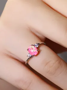 Vista macro di un anello d'argento con opale rosa ovale con riflessi di fuoco e pietre laterali