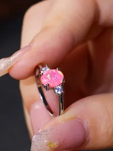 Vista macro di un anello con opale rosa ovale e zirconi tenuto tra le dita