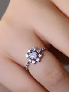 Dettaglio di un anello a fiore con opale e petali di zircone indossato da una modella