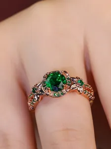 Detail of rose gold ring featuring a large green round gemstone and intricate hollow band