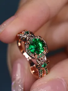 Detailed close-up of rose gold ring featuring a large round green gem and hollowed leaf band