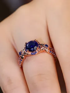 Detailed close-up of rose gold ring with round blue gemstone and pavé accents
