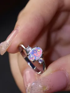 Dettaglio macro di un anello con opale ovale, pietre laterali e riflessi vivaci