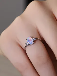 Dettaglio anello con opale ovale e diamanti laterali in argento su mano di modella